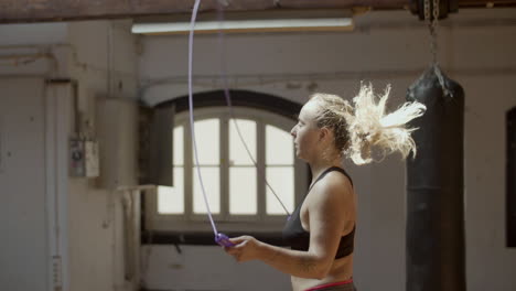 Side-view-of-young-serious-woman-jumping-rope-in-gym
