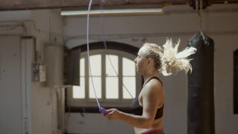 side view of young serious woman jumping rope in gym