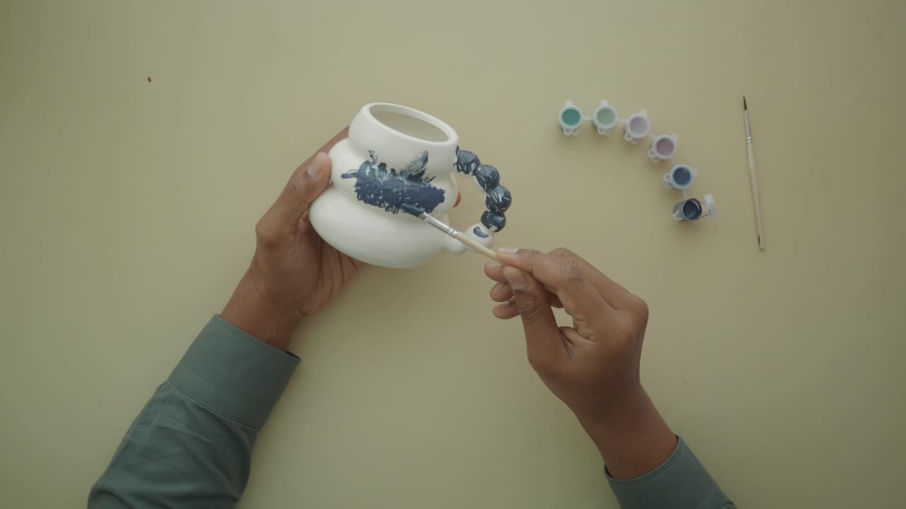 Person's Hands Painting a Ceramic Mug with Blue Paint
