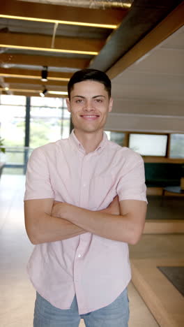 vertical video: smiling man standing with arms crossed in modern office hallway