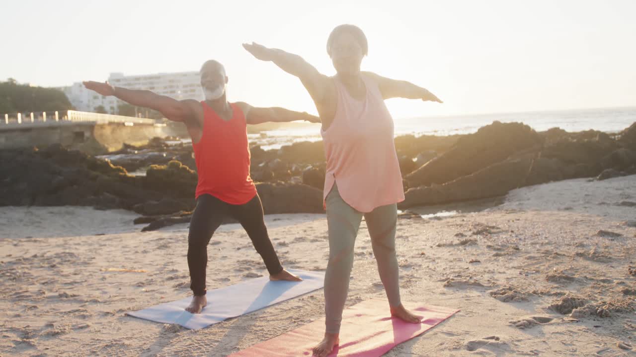 Lykkelig eldre afroamerikansk par driver med yoga, tøyer ut på stranden, sakte film