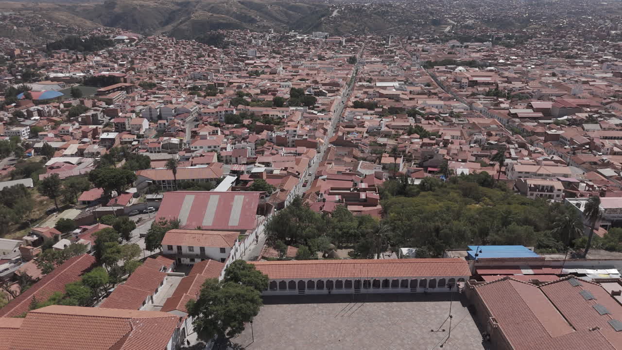 Wide drone shot of Sucre Bolivia on a bright day with blue sky starting over the square on top of the city LOG
