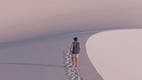 aerial shot orbit view a boy or a man walking alone in the white sand dunes with a lagoon of the lencois maranhenses in maranhao, brazil. unesco world heritage site. establishing shot. footprints.
