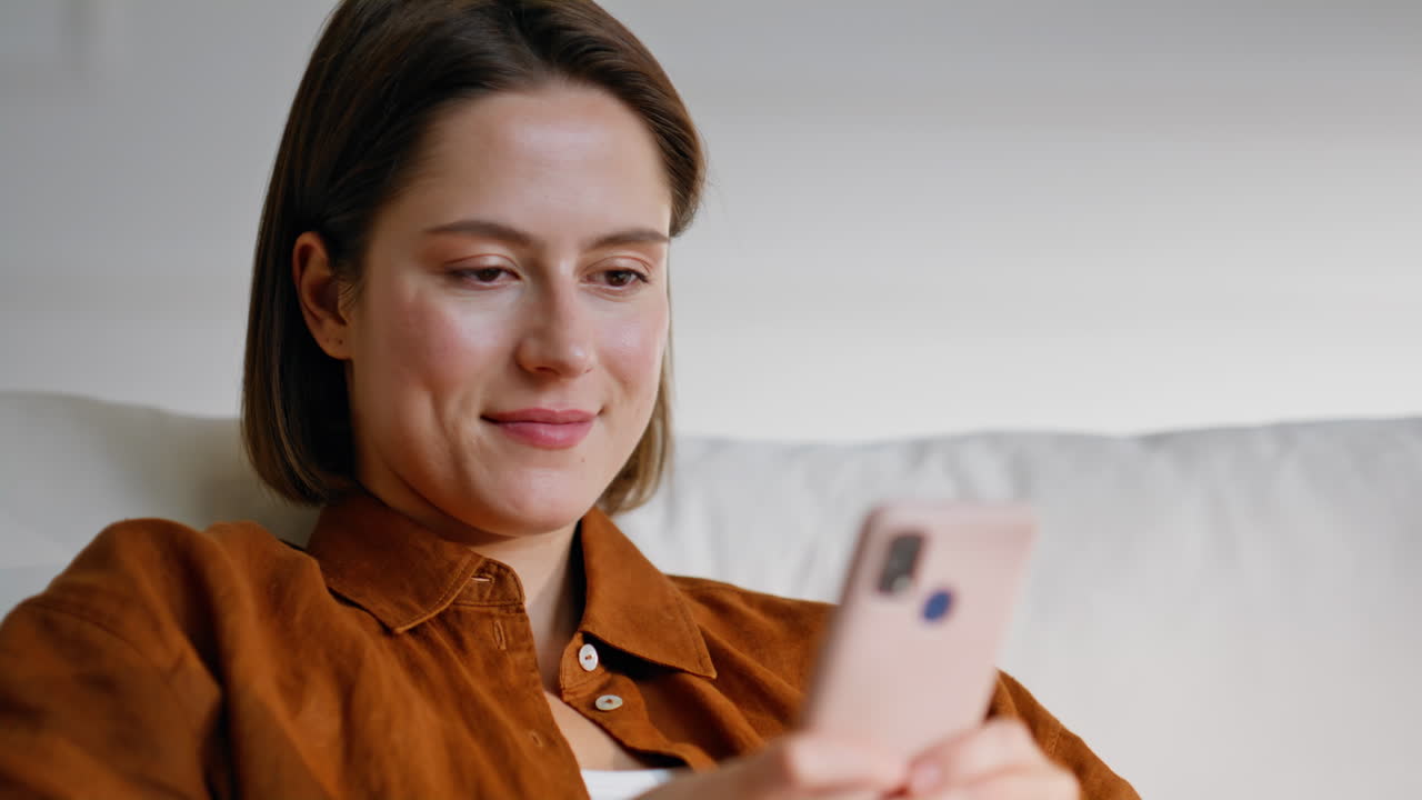 Closeup girl texting mobile phone lying on comfortable couch. Smiling woman