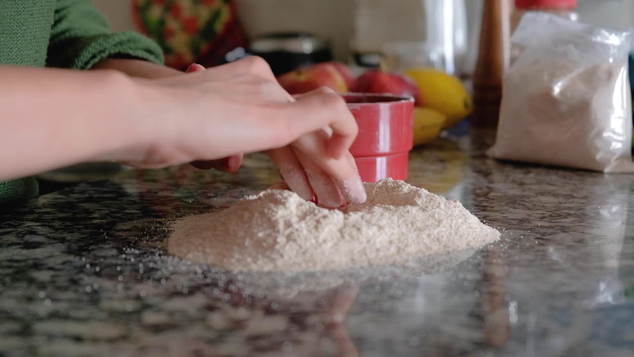 조리대 위에 밀가루를 붓고 가운데에 구멍을 뚫는 여자
