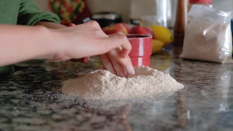 woman pouring flour over the countertop and making a hole in the middle