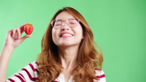 young woman enjoying strawberry in studio with green screen chroma key background