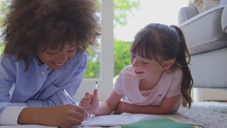 boy and girl lying on rug in lounge at home doing school homework together