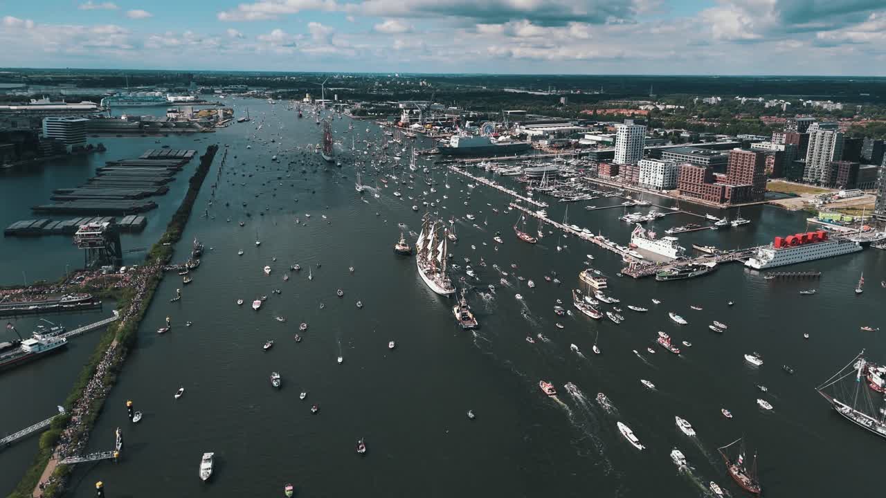 High drone orbit right showing boats exiting harbor at end of Amsterdam Sail festival, rearview