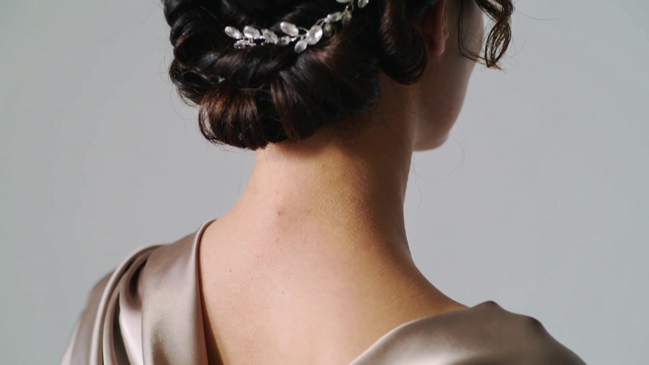 La cámara se aleja revelando a una modelo femenina apoyada en un estudio, mostrando una espalda de satén con cuello desbocado y una enredadera de cristal.