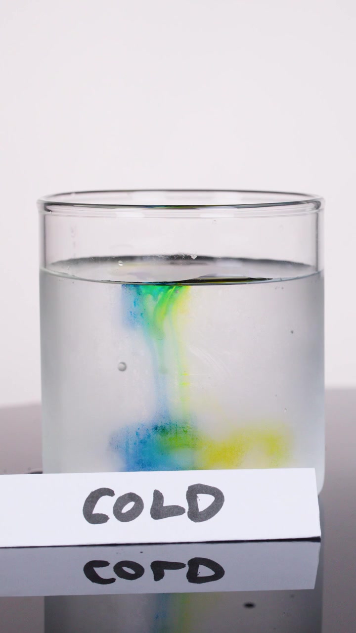 Tinte de color se dispersa lentamente en un vaso de agua fría, capturado con cámara estática e iluminación brillante