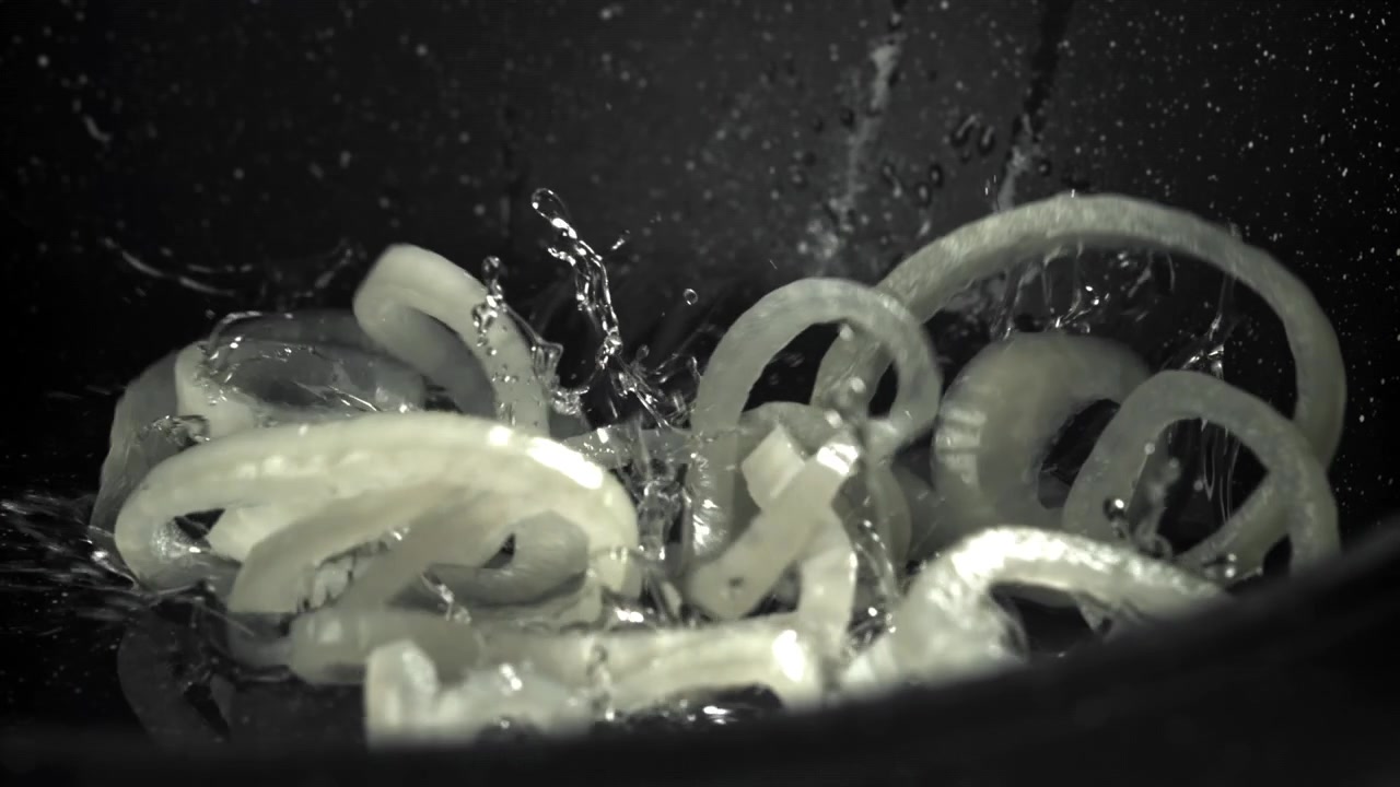 Slowmotion nærbillede af løgringe, der falder ned i varm olie på en pande