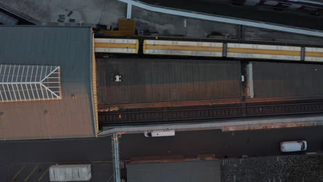 Yellow-Train-entering-Subway-Station-elevated-above-ground-in-Berlin,-Germany-from-Aerial-Birds-Eye-Overhead-Top-Down-View-perspective