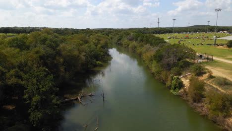 Aerial-view-of-river-that-runs-through-community,-creek-surrounded-by-golf-course-and-sports-fields,-drone-4K