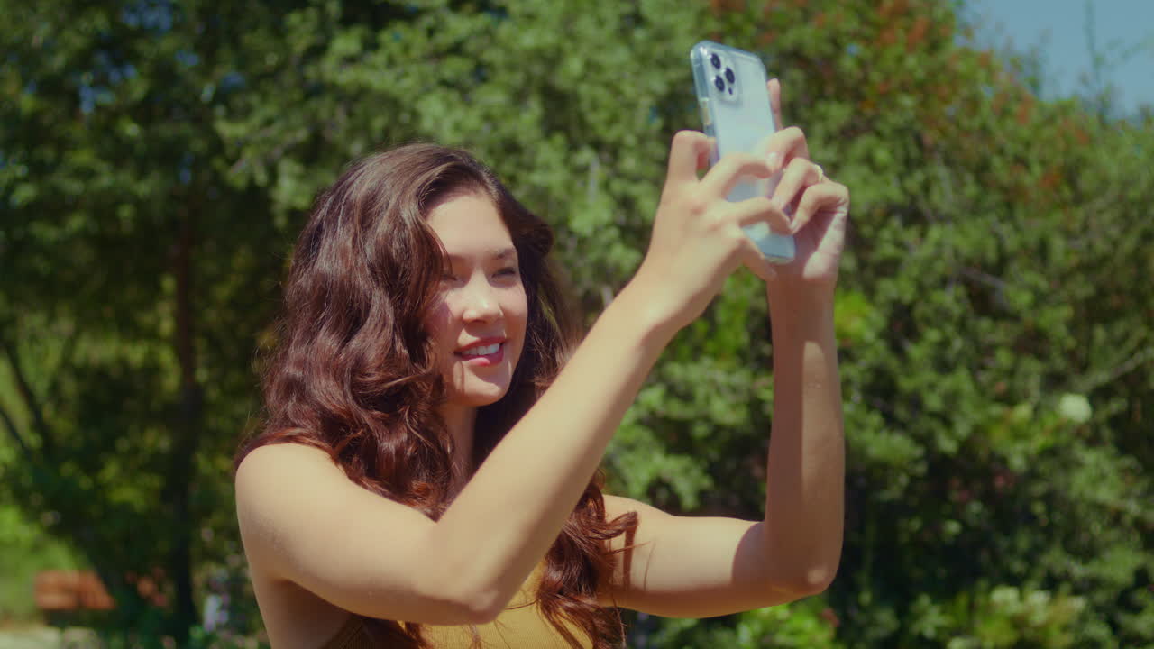 Menina asiática fotografando a paisagem no parque em close-up. Mulher usando um smartphone.