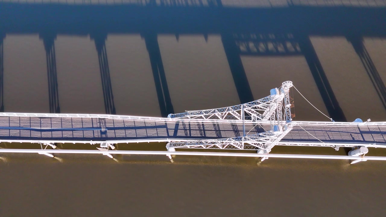 Top-down aerial view of a truss bridge casting long shadows over the Clarence River.