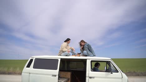 two young girls play chess on the roof of a caravan on a road lost in the middle of the countryside.