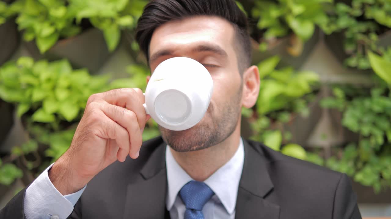 un primer plano de un apuesto hombre de negocios sonriente en traje formal bebiendo una taza de café.