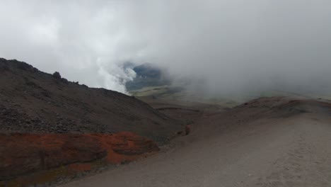 a mist covered ridge on cotopaxi volcano, ecuador, showing steep slopes and rocky volcanic ground, empty sand dirt path