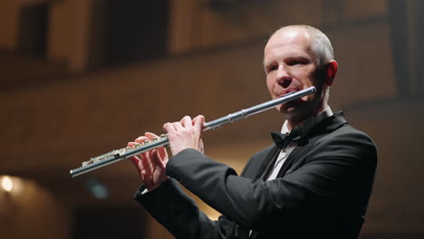 portrait of aged man with flute on scene of old music hall or opera house talented musician is performing party