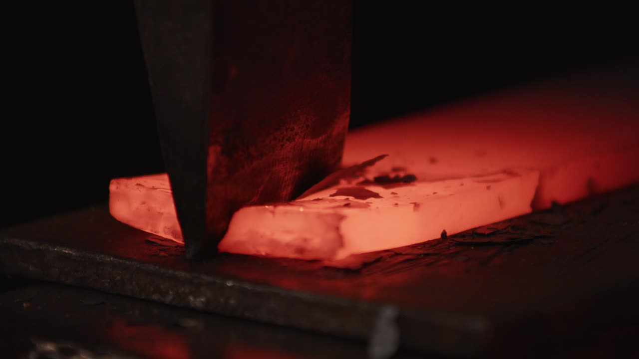 Scale flies off red hot glowing piece of iron being hit by chisel on anvil