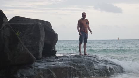 happy male tourist standing on coastal rock and gesturing thumbs-up at dam trau beach in vietnam