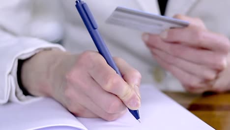 woman-writing-notes-with-a-pen-at-a-office-table-holding-payment-credit-card-with-people-stock-video-stock-footage