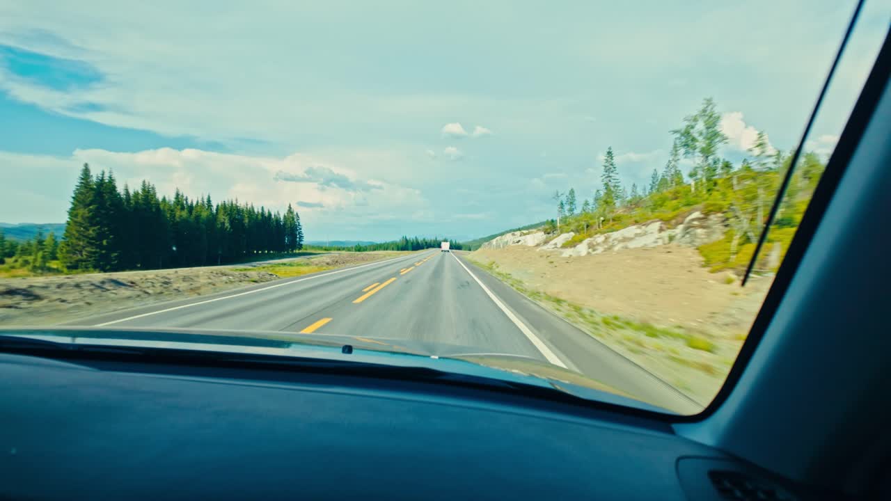 Guidando lungo un ampio tratto di strada aperto con alberi sparsi e colline distanti sotto un cielo luminoso, E6 Nord da Fosen, Trøndelag, Norvegia - Ripresa POV.