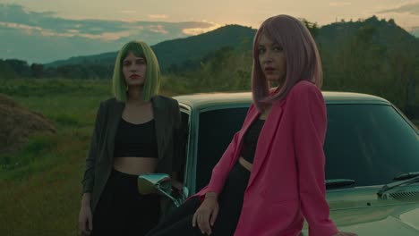 two stylish women posing beside a vintage car at sunset