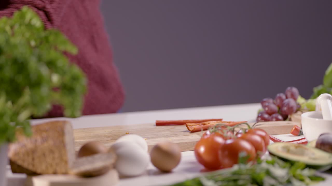 Slow-motion close-up of a chef wiping a wooden cutting board and knife. Black gloves ensure hygiene, while fresh ingredients like tomatoes, herbs, and bread create a professional kitchen setting