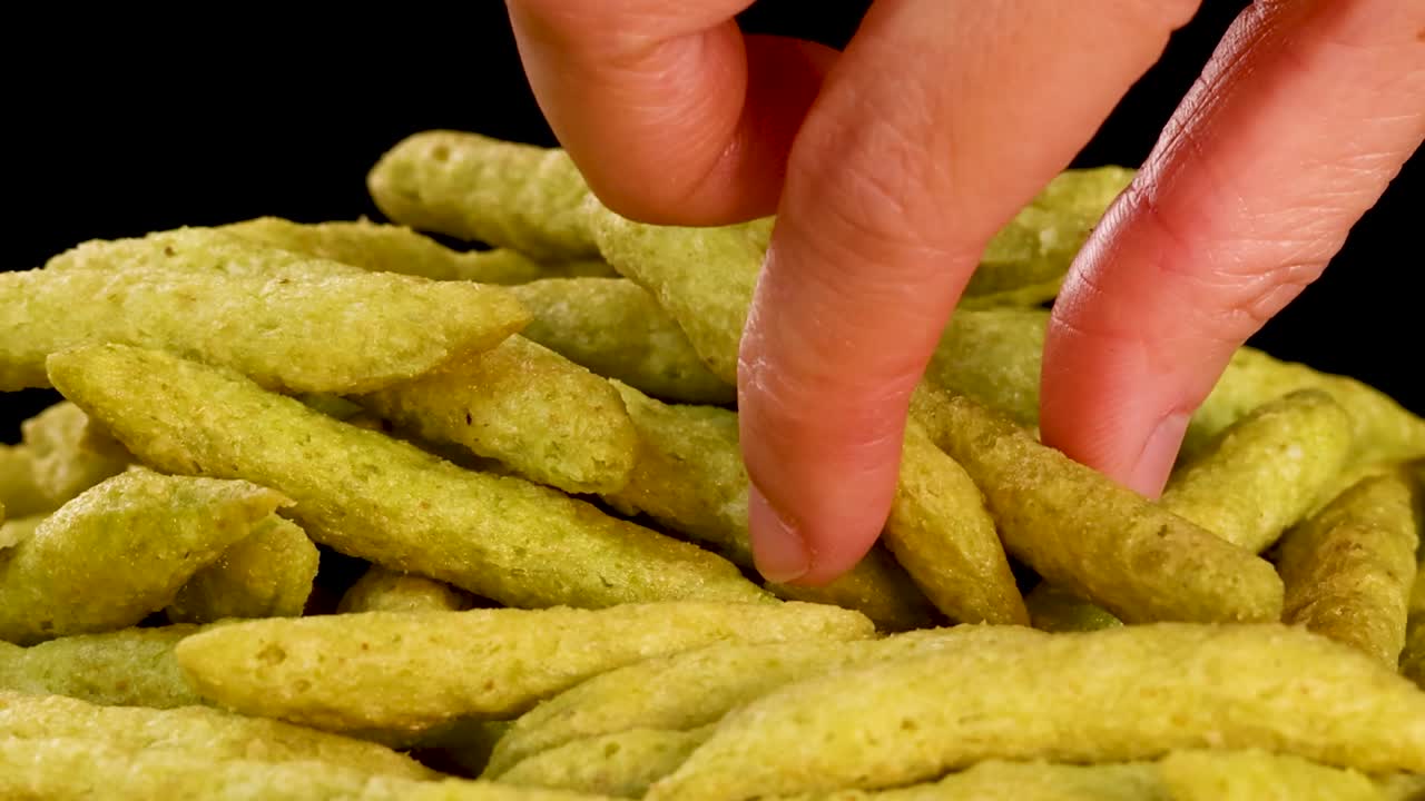 Nærbilde av fingre som velger en sprø, grønn ert snack fra en haug mot svart bakgrunn