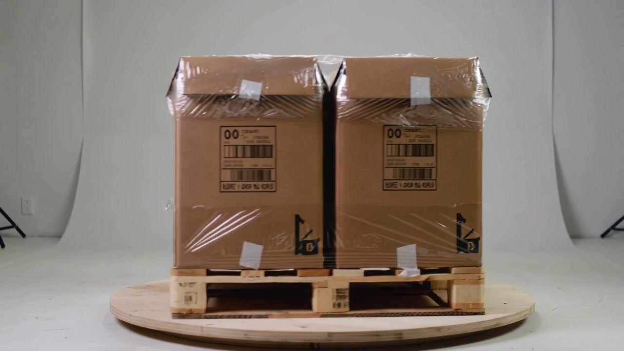 Rotating wooden turntable carrying pallet load showing barcodes while shrinkwrap curling in studio