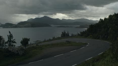 young man cycling uphill in dark, moody, windy weather, storm brewing, with fully packed touring bike