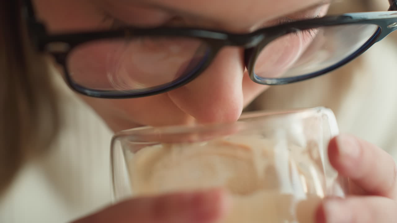 extreme close up of student holding warm beverage in transparent cup, foam texture swirls on surface, soft natural lighting with minimal background