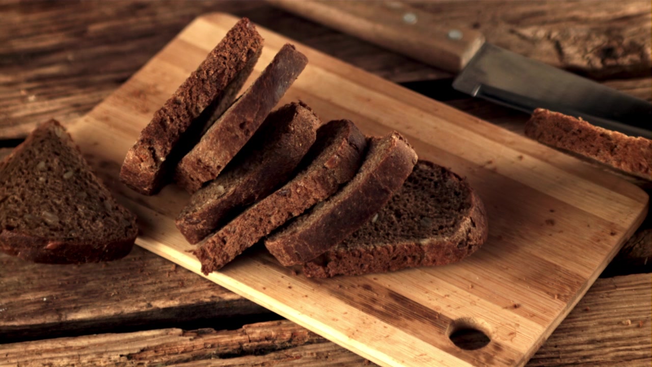 Fatias de Pão de Centeio Caindo sobre uma Tábua de Corte de Madeira