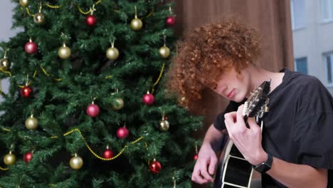 person playing acoustic guitar next to a decorated christmas tree