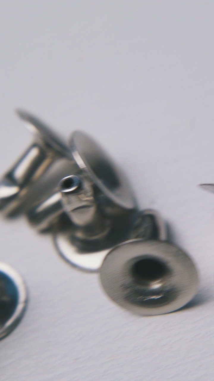 small pile of scattered shiny metal rivets lies at random on clean light surface extreme close view