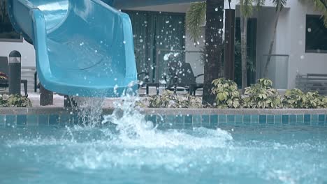 Fröhlicher-Junge-Reitet-In-Zeitlupe-Des-Hotels-Auf-Der-Wasserrutsche-In-Den-Pool