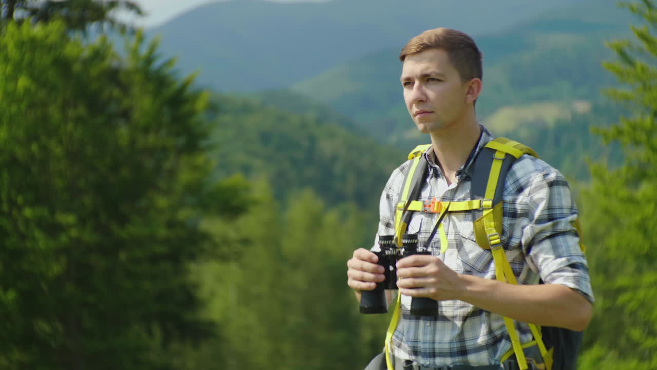 배낭을 메고 있는 한 남자가 백그룬에 대한 쌍안경 백뷰를 통해 앞을 내다본다