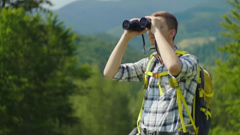 un hombre con una mochila mira hacia adelante frente a él a través de la vista posterior de los binoculares contra el fondo