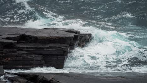 heavy waves hit the dark jagged rocks on the shoreline