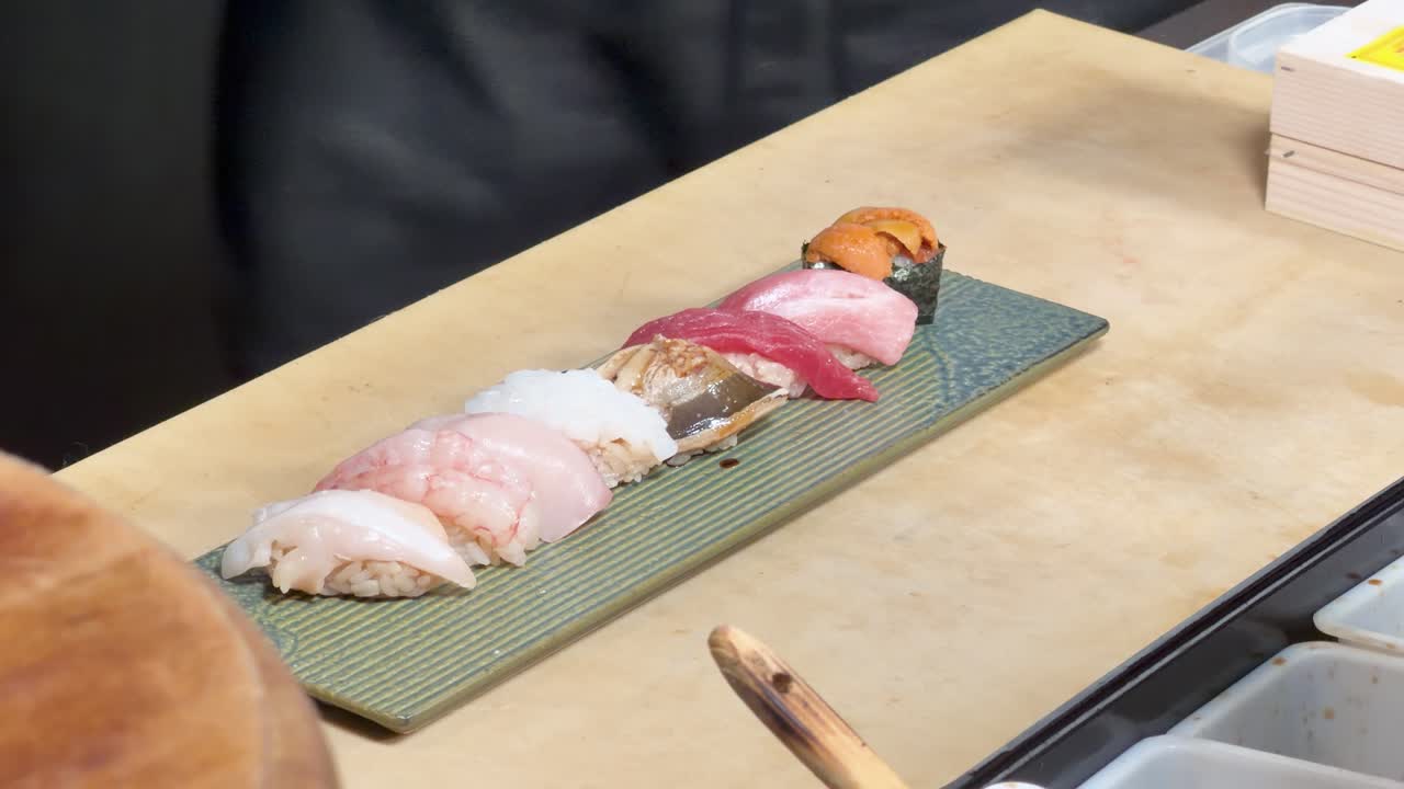 Detailní záběr kuchaře, který štětcem potírá omáčkou různé nigiri sushi na pultu, statický záběr shora