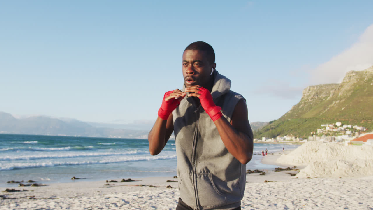 Focused african american man boxing, exercising outdoors by the sea
