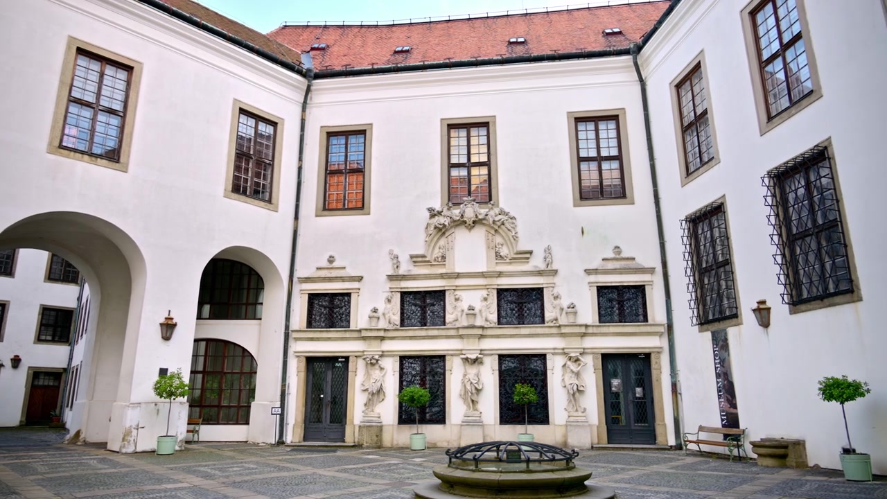 Cichy dziedziniec zamkowy z rzeźbionym portalem i arkadami wokół drzew w donicach, Mikulov, Czechy