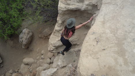 Vista-De-Arriba-Hacia-Abajo-De-Una-Joven-Excursionista-Escalando-Un-Acantilado-Rocoso-En-El-Desierto-Del-Territorio-Navajo,-Nuevo-México,-Estados-Unidos,-Cámara-Lenta-De-Marco-Completo