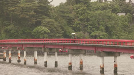 Rote-Brücke-In-Der-Matsushima-Bucht-Zur-Insel-Fukuura-Mit-Einem-Paar,-Das-Mit-Sonnenschirmen-Spazieren-Geht