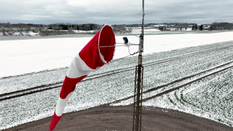 a revealing shot of a red and white windsock on a small snow-covered airfield, captured in the northern part of denmark