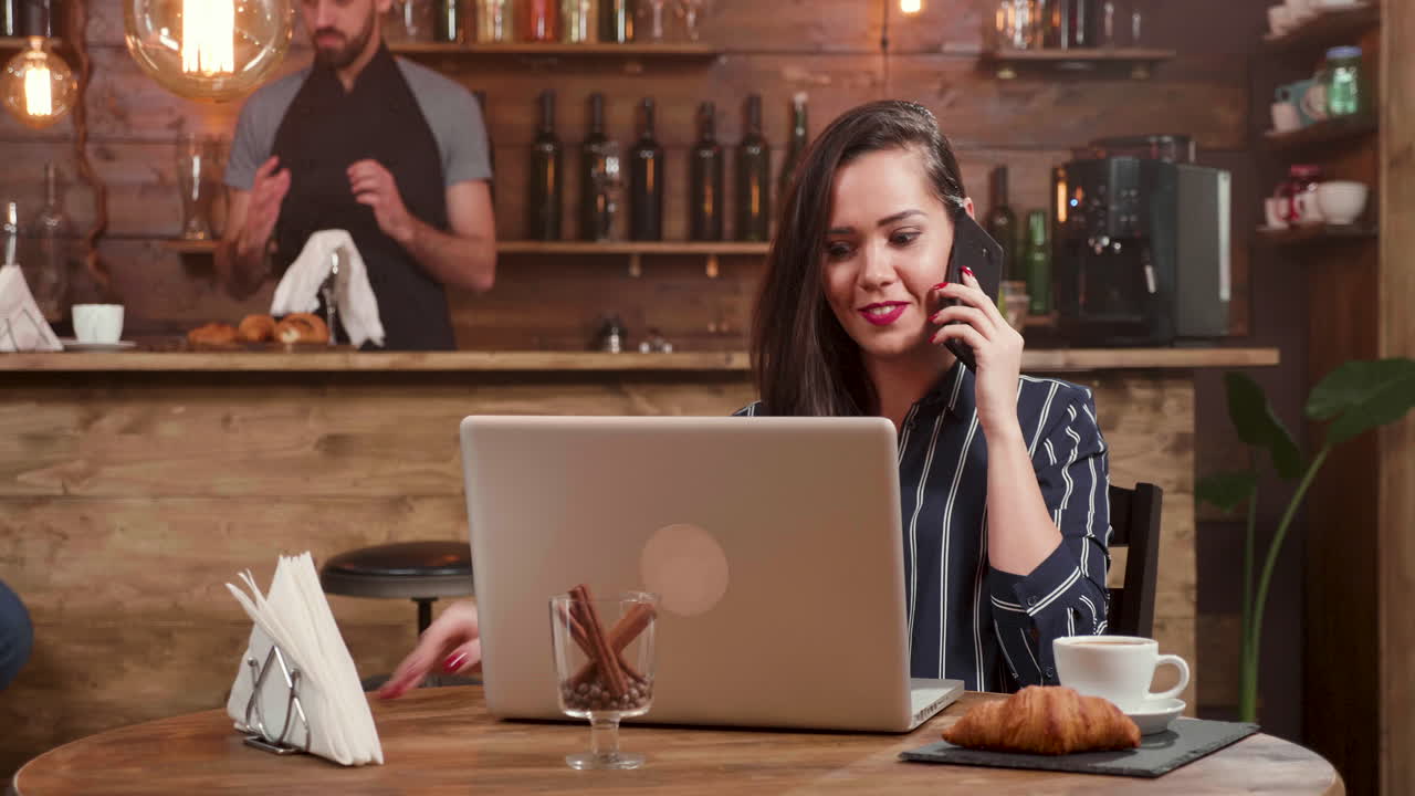 Woman working on laptop at cafe while talking on the phone