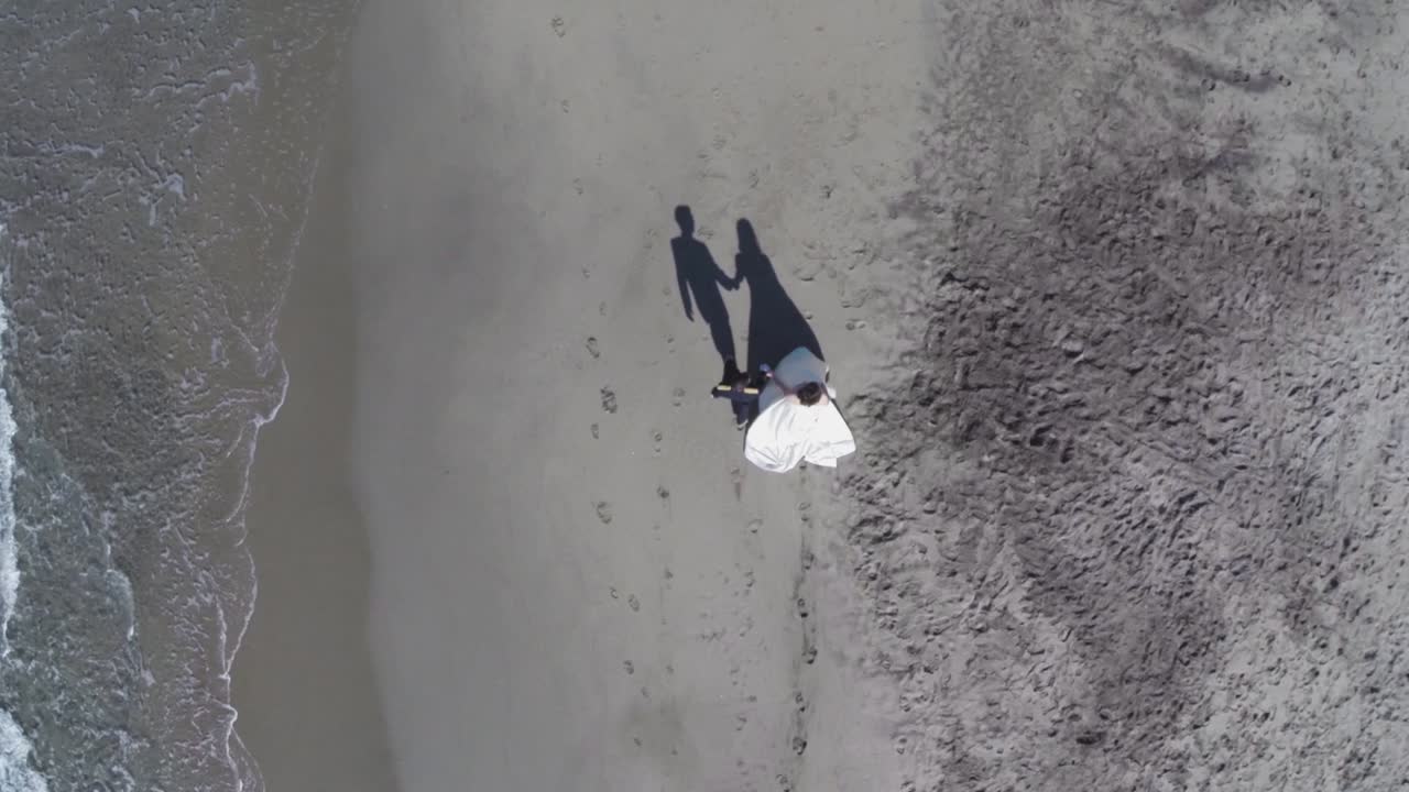 화창한 날 해변을 따라 손을 잡고 걷는 젊은 군인과 그의 아내의 항공 이미지, 해변의 모래에 부서지는 파도