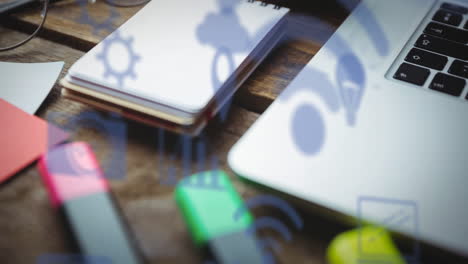 Animation-of-multiple-digital-icons-against-close-up-of-office-equipment-on-wooden-table